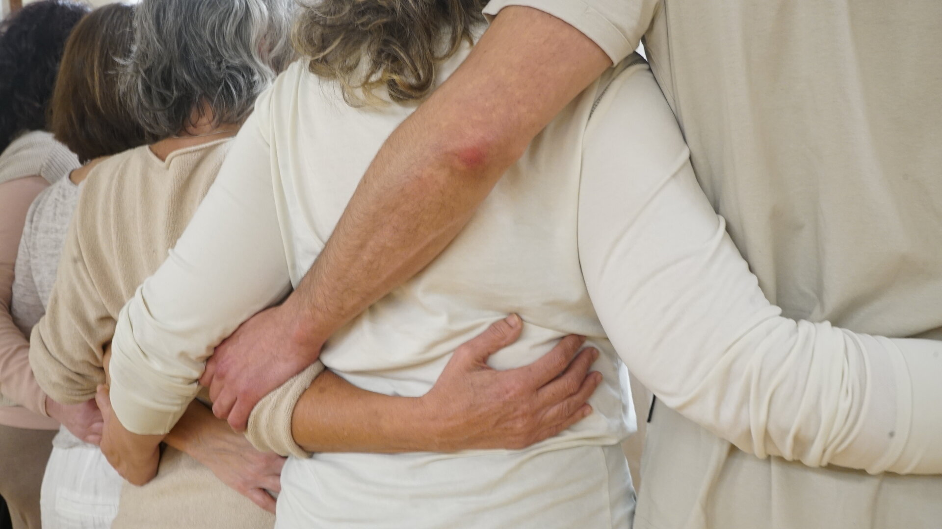 Personas abrazándose en círculo en un entorno interior, gesto de apoyo y conexión grupal